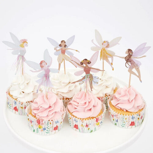 Zes cupcakes met feeën toppers en gebloemde cupcakevormpjes, met witte en roze frosting.