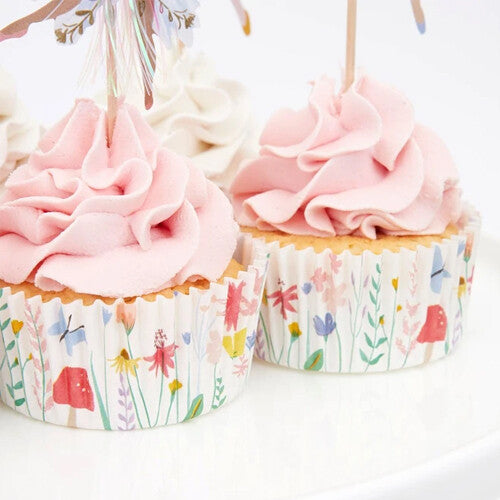 Twee cupcakes met roze frosting en gebloemde cupcakevormpjes, met een feeën topper.
