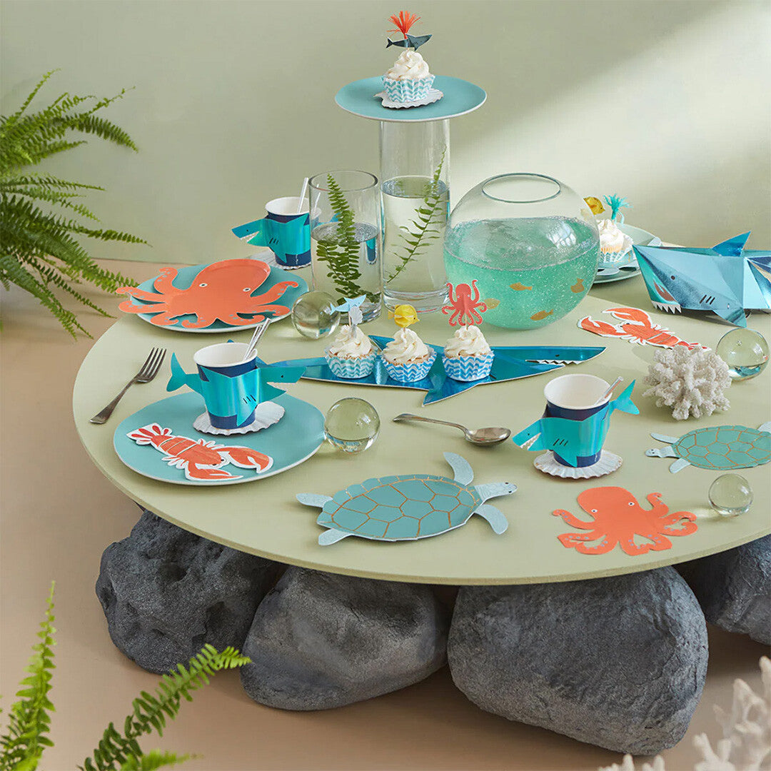 Een feestelijk gedekte tafel met Meri Meri onderwater thema cupcake decoraties en bijpassende borden en bekers.