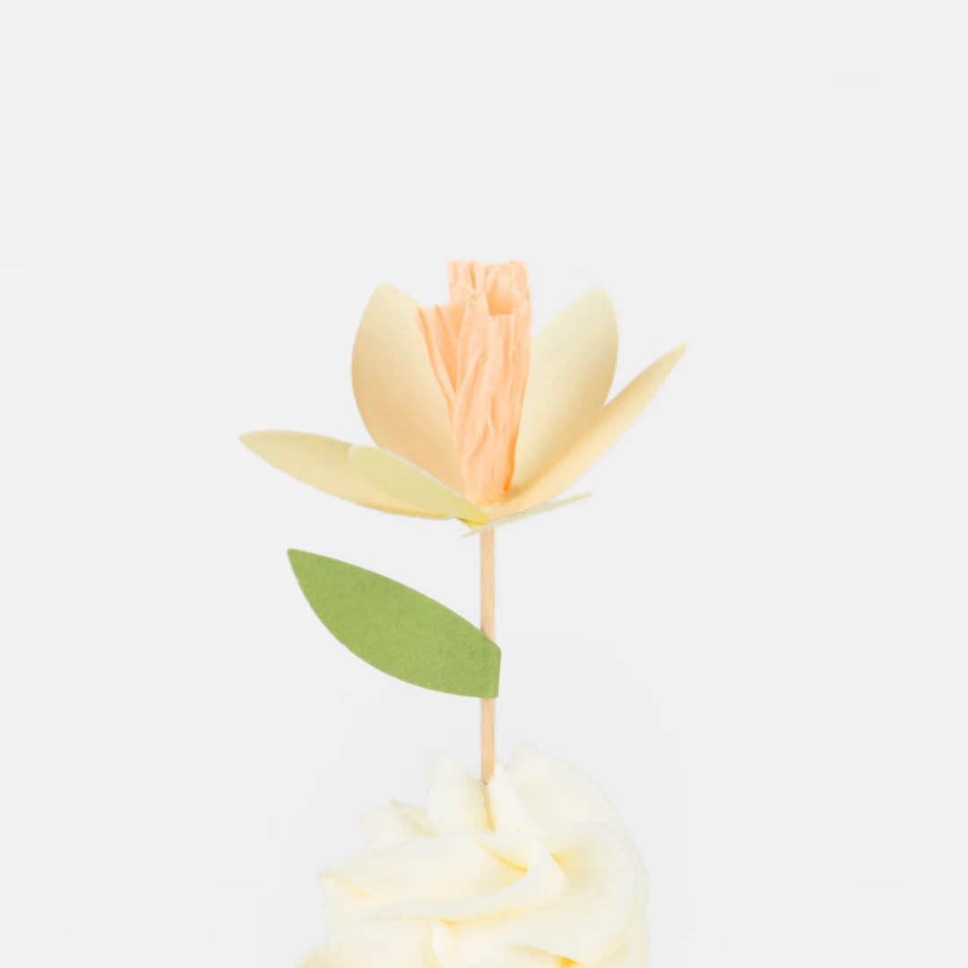 Detailfoto van een cupcake met een gele bloemtopper en een groen blad.
