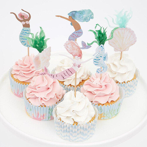 Zes versierde cupcakes met zeemeerminnen en onderwater thema toppers op een witte schaal.