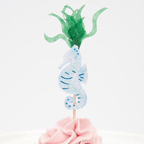 Detail van een lichtblauw zeepaardje cupcake topper met groen zeewier.