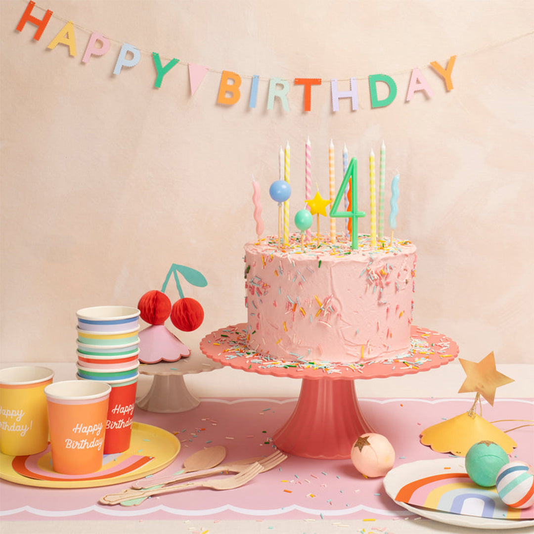 Een feestelijk gedekte tafel met een roze verjaardagstaart versierd met kleurrijke kaarsen en een 'Happy Birthday' slinger.