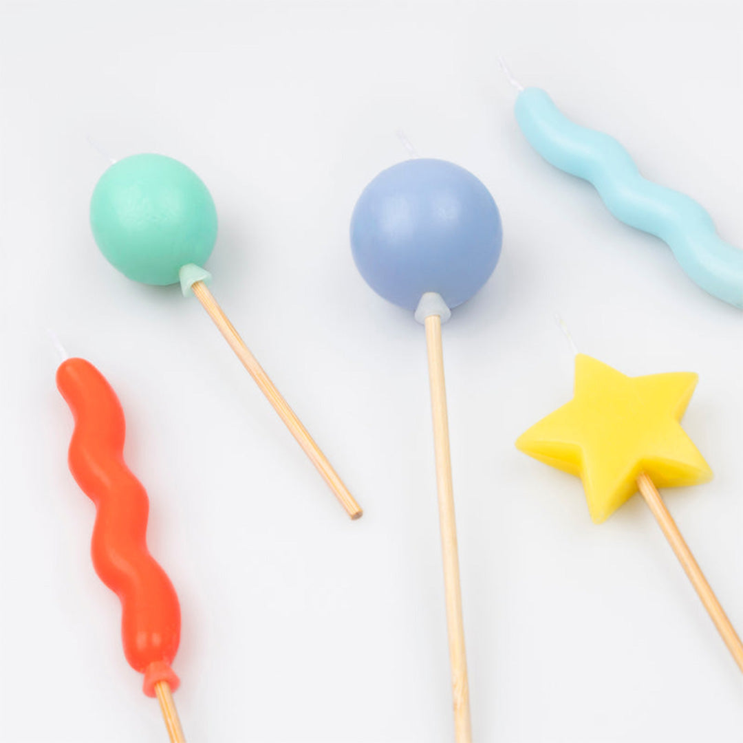 Detailopname van vijf kleurrijke Meri Meri verjaardagskaarsen in de vormen van golven, ballonnen en een ster.