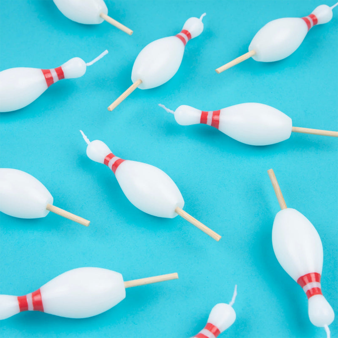 Meerdere witte verjaardagskaarsjes in de vorm van bowlingkegels met rode strepen, verspreid over een blauwe ondergrond.