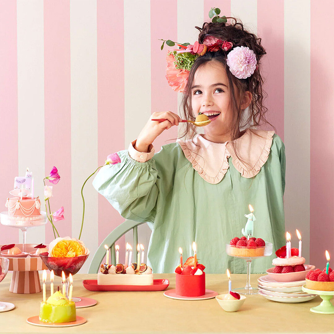 Meisje eet taart aan een feestelijk gedekte tafel met kleine taartjes en brandende verjaardagskaarsjes.