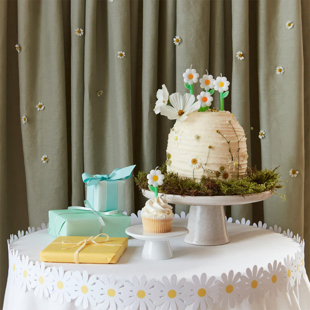 Een feestelijk gedekte tafel met een taart en cupcake versierd met madeliefjeskaarsjes en cadeautjes.