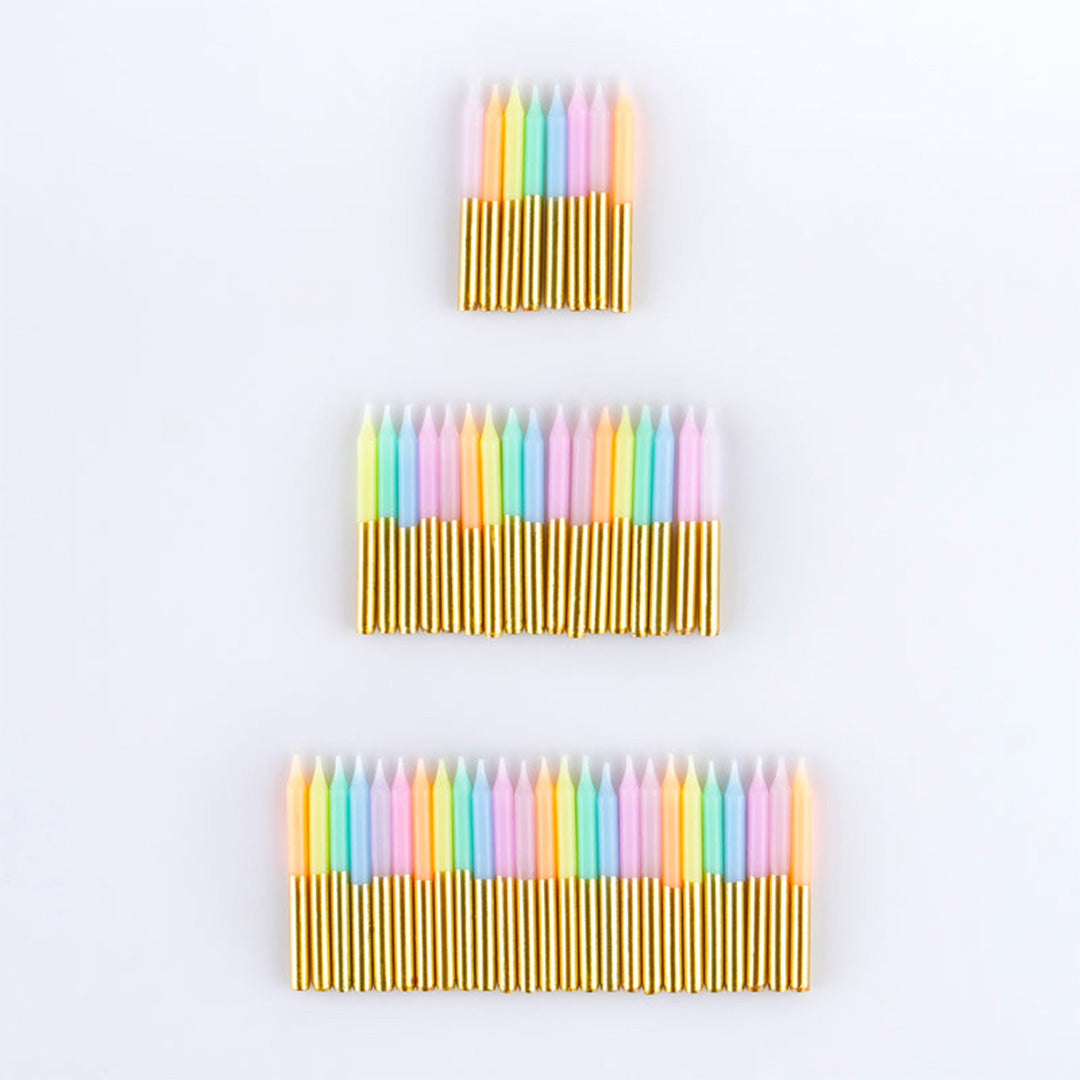 Drie groepen pastelkleurige verjaardagskaarsen met gouden voetjes, van klein naar groot gerangschikt.