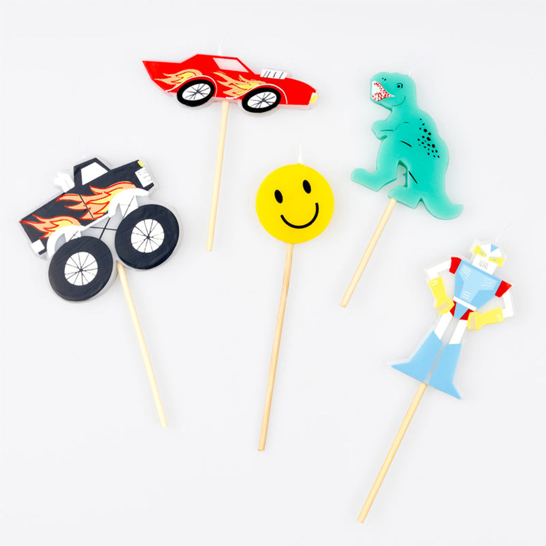 Meri Meri set van vijf verjaardagskaarsen in de vorm van een raceauto, dinosaurus, smiley, robot en monstertruck, schuin van bovenaf gezien.