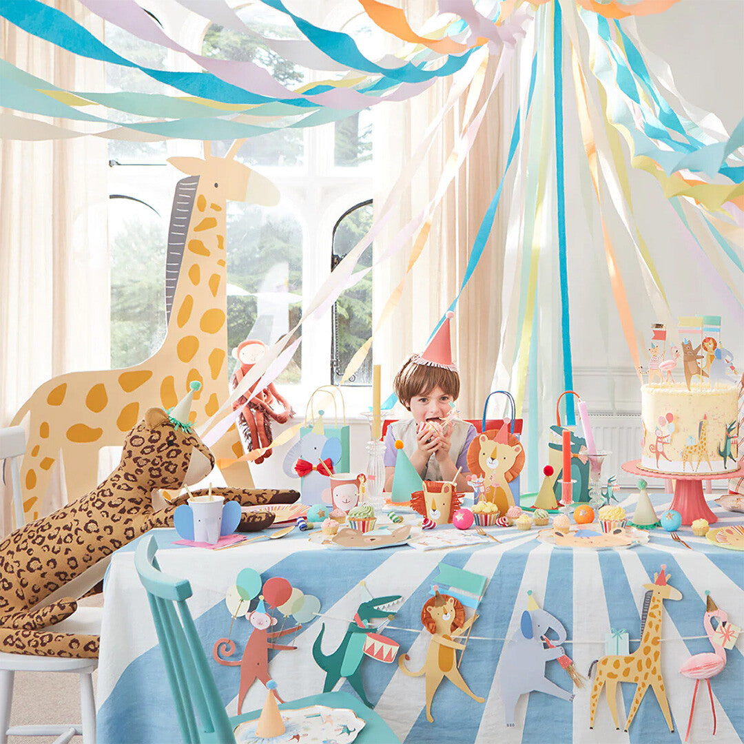 Een feesttafel met een kind, versierd met Meri Meri Animal Parade feestdecoratie en cadeautasjes.