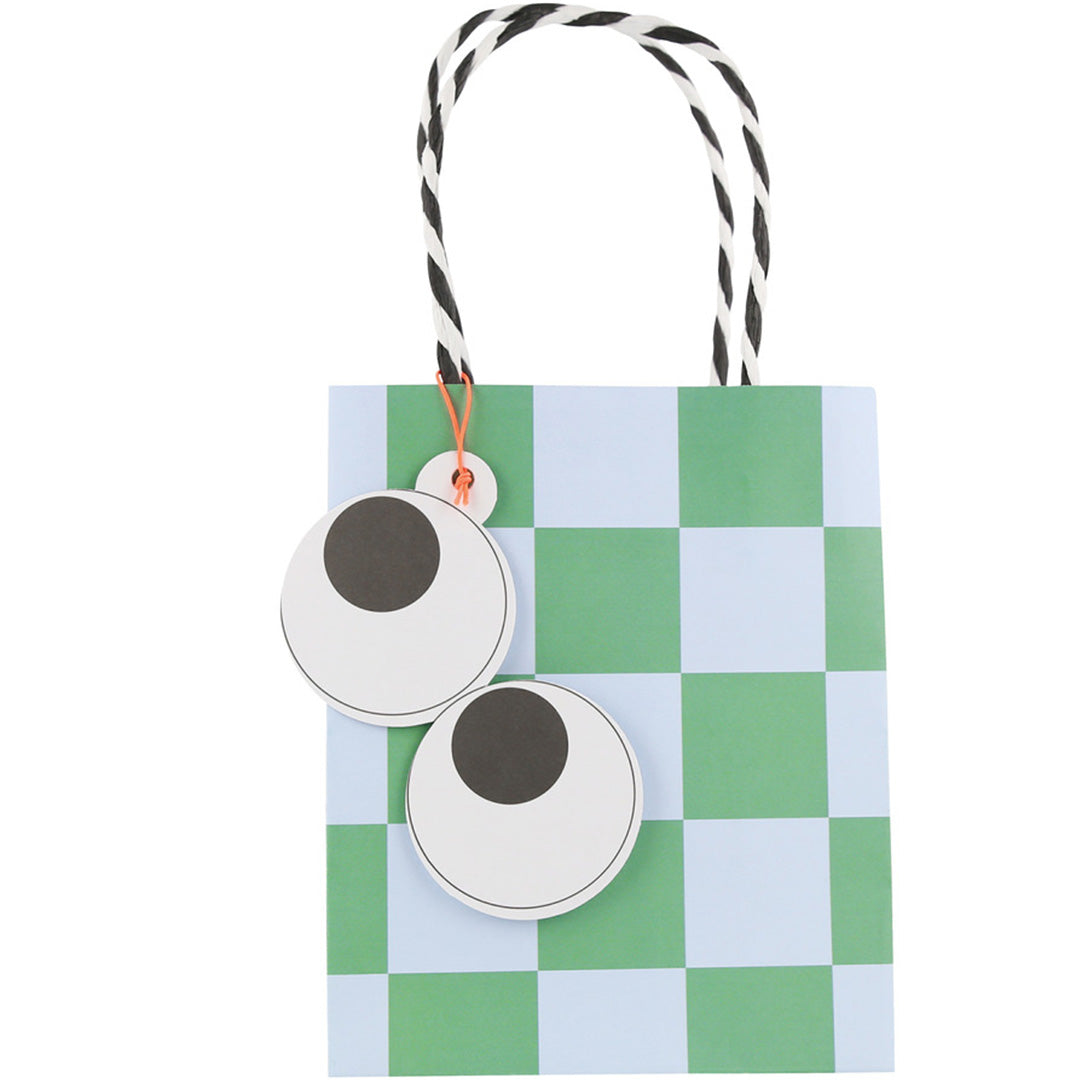 Een Meri Meri feesttasje met een groen-blauw geruit patroon en twee grote googly eyes.