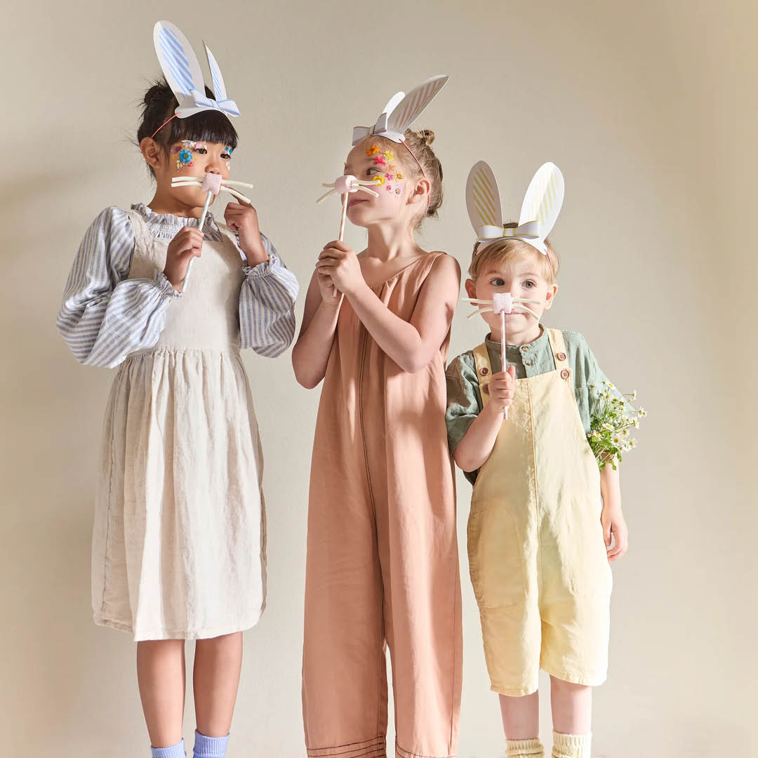 Drie kinderen dragen Meri Meri gestreepte konijnenoren en houden konijnenneusjes vast.