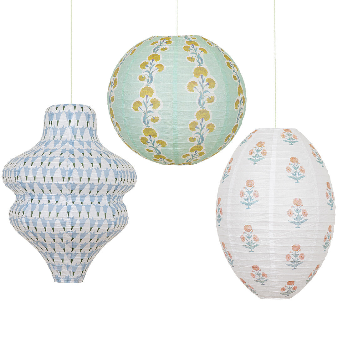 Drie Meri Meri papieren lampionnen in verschillende vormen en gebloemde of geometrische patronen, geïsoleerd op een witte achtergrond.