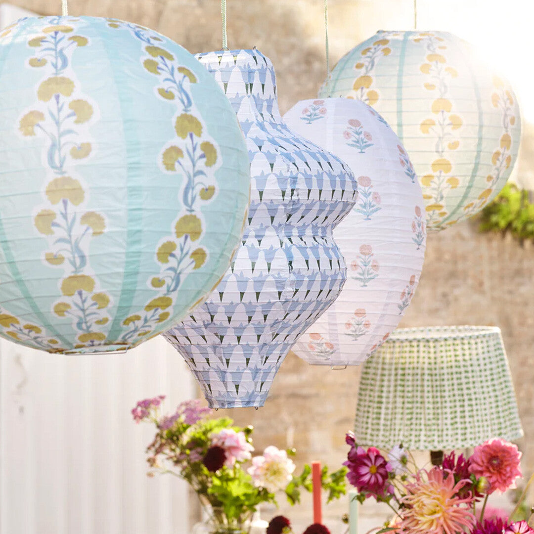 Vier Meri Meri papieren lampionnen hangen buiten boven een feestelijk gedekte tafel met bloemen.