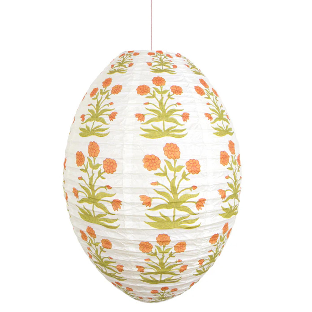 Een enkele Meri Meri eivormige papieren lampion met oranje gebloemd patroon hangt geïsoleerd.