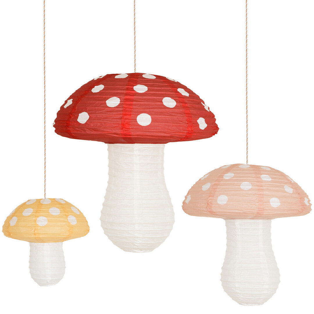 Drie Meri Meri papieren paddenstoel lampionnen in rood, geel en lichtroze hangen naast elkaar.