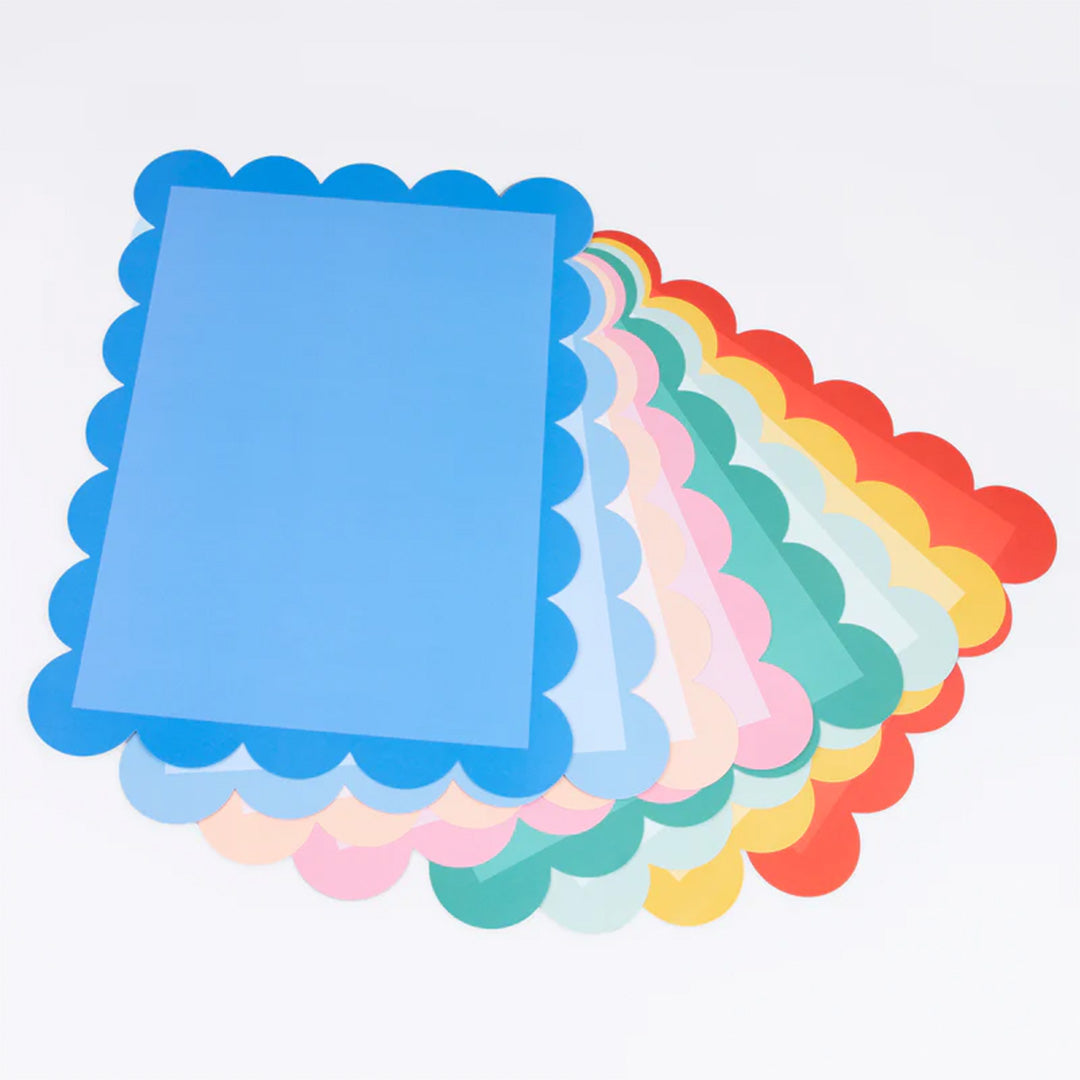 Een waaier van meri meri placemats in diverse kleuren met geschulpte randen, schuin van bovenaf gefotografeerd.