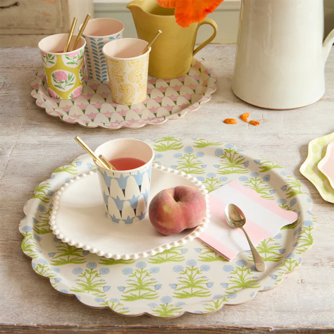 Tafelsetting met twee Meri Meri serveerschalen, één met roze bloemen en één met blauwgroen bloemenpatroon, met servies en fruit.