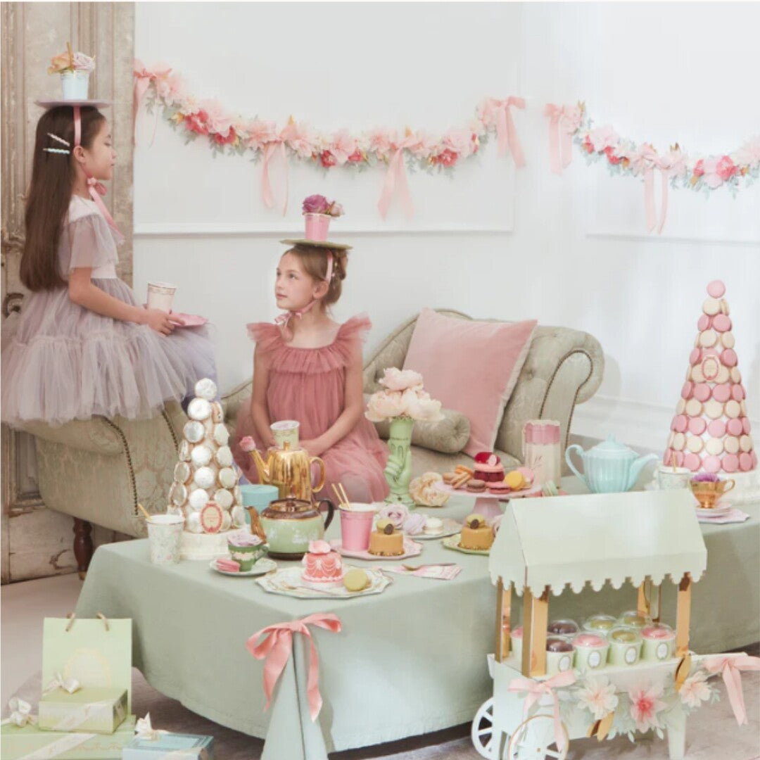 Twee meisjes aan een feestelijk gedekte tafel met Meri Meri Ladurée Paris Floral servetten en andere theeparty decoraties.