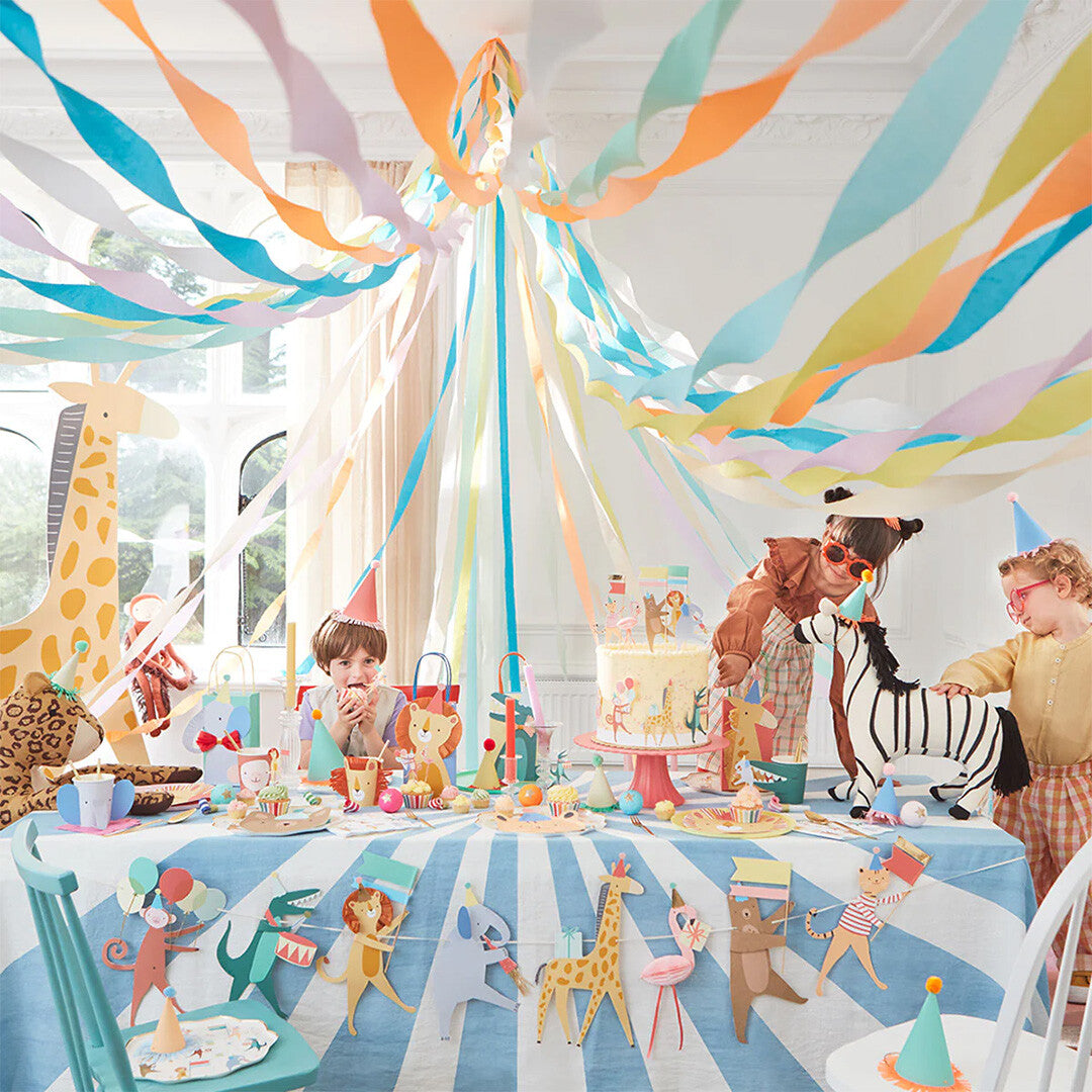 Een feestelijk versierde kamer met de Meri Meri dierenparade feestslinger onder een tafel, omringd door kinderen en andere feestdecoraties.