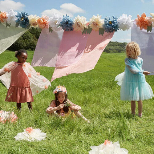 Drie kinderen spelen in een veld met de Meri Meri bloemenslinger op de achtergrond.