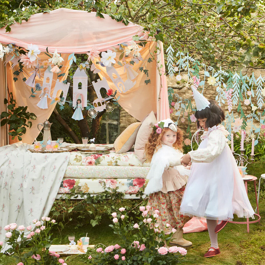 Twee meisjes spelen in een sprookjesachtige tuin met de Meri Meri prinsessenslinger als decoratie.