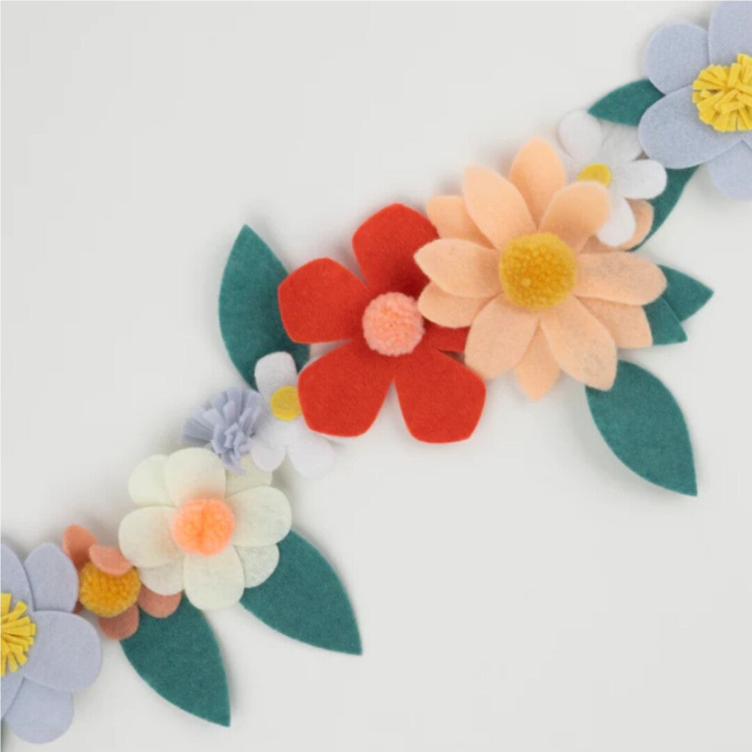 Close-up van de vilten bloemenslinger met oranje, perzikkleurige en witte bloemen met pompons.