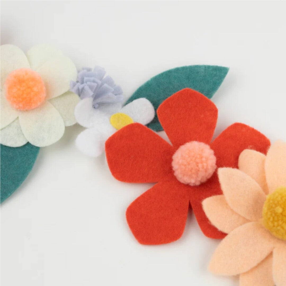Close-up van de vilten bloemenslinger met rode, perzikkleurige en witte bloemen met pompons.