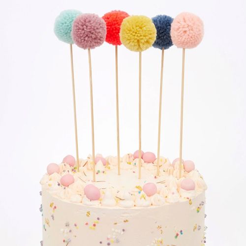 Meri Meri pompom taartversiering op een witte taart met sprinkles.