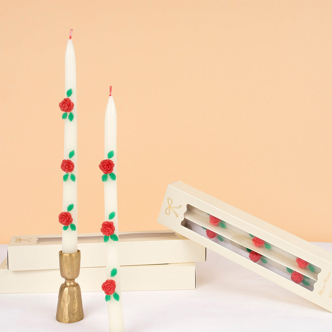 Twee Meri Meri beige conuskaarsen met rozen, waarvan één in een gouden kandelaar, naast twee verpakkingen.