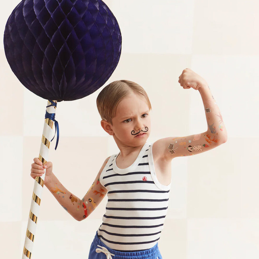 Kind met Meri Meri tijdelijke tatoeages op de armen, een snorretje en een grote blauwe decoratiebal.