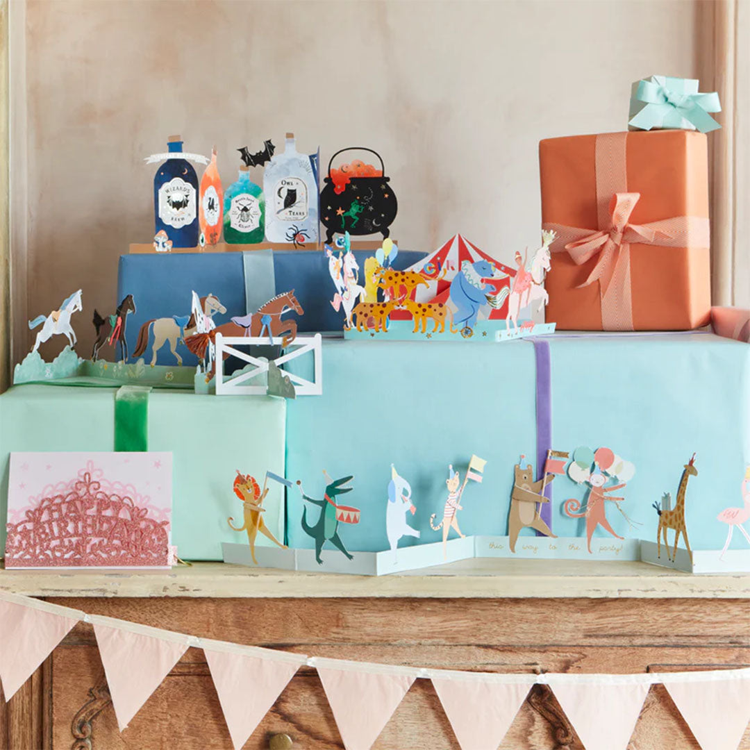De meri meri verjaardagskaart met dierenparade als onderdeel van een feestelijke decoratie op een plank met cadeaus.