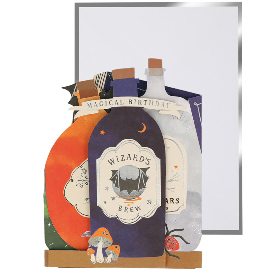 Meri meri pop-up verjaardagskaart met toverdrankflesjes en een witte envelop, van voren gezien.