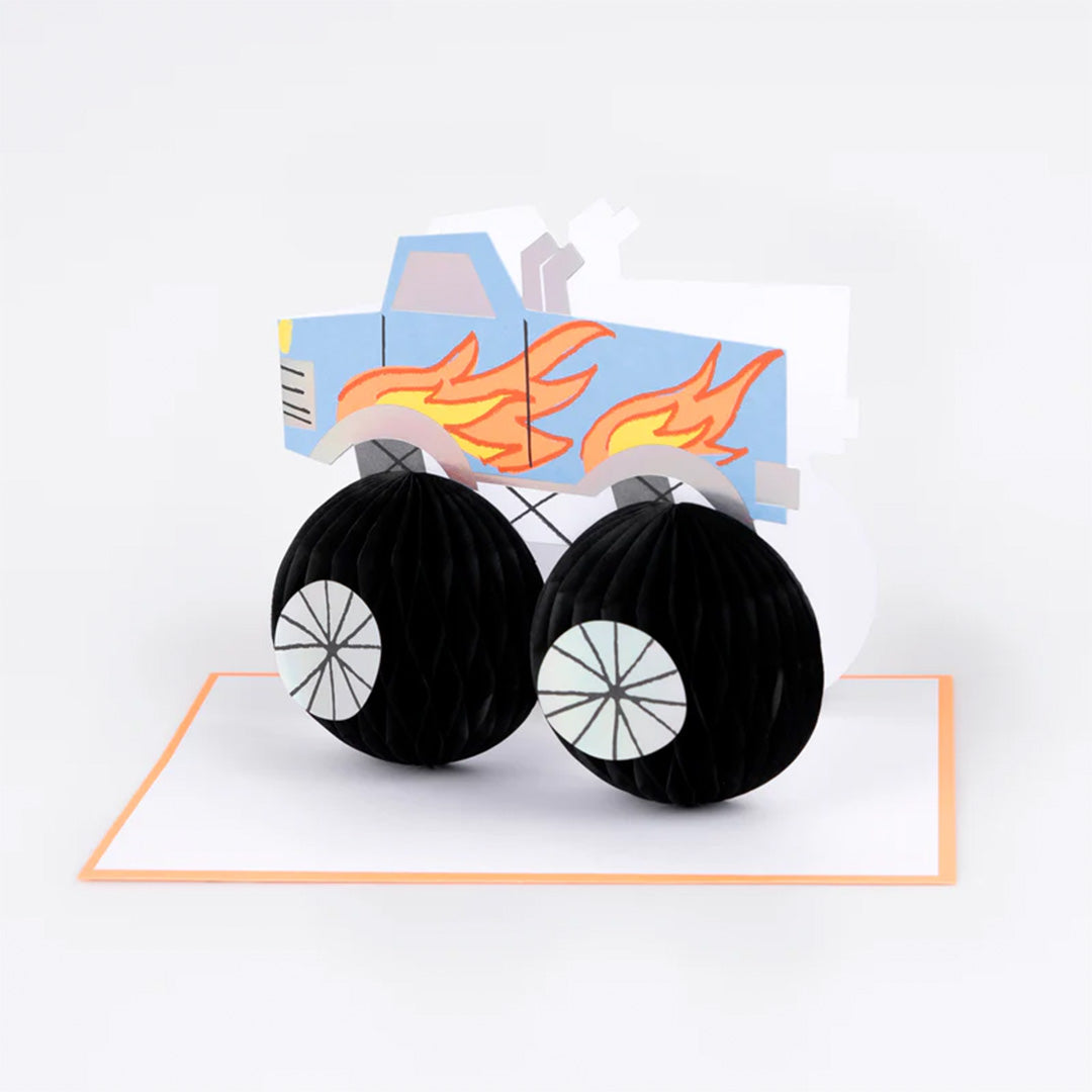 Meri Meri verjaardagskaart met een blauwe monster truck en zwarte honingraatwielen, half open op een witte ondergrond.