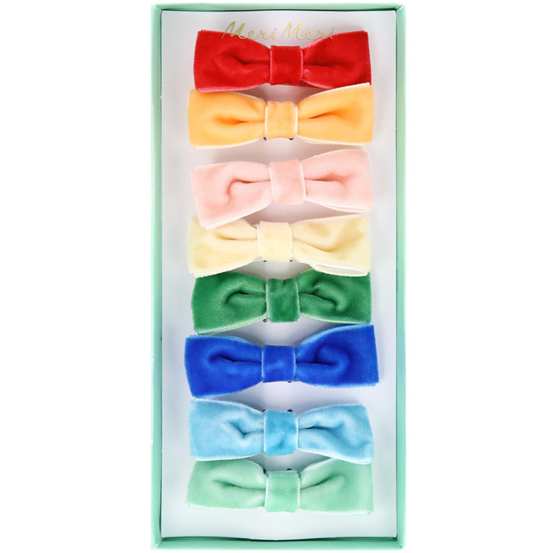 De Meri Meri set van acht fluwelen haarclips in regenboogkleuren, gepresenteerd in een lichtgroene verpakking.