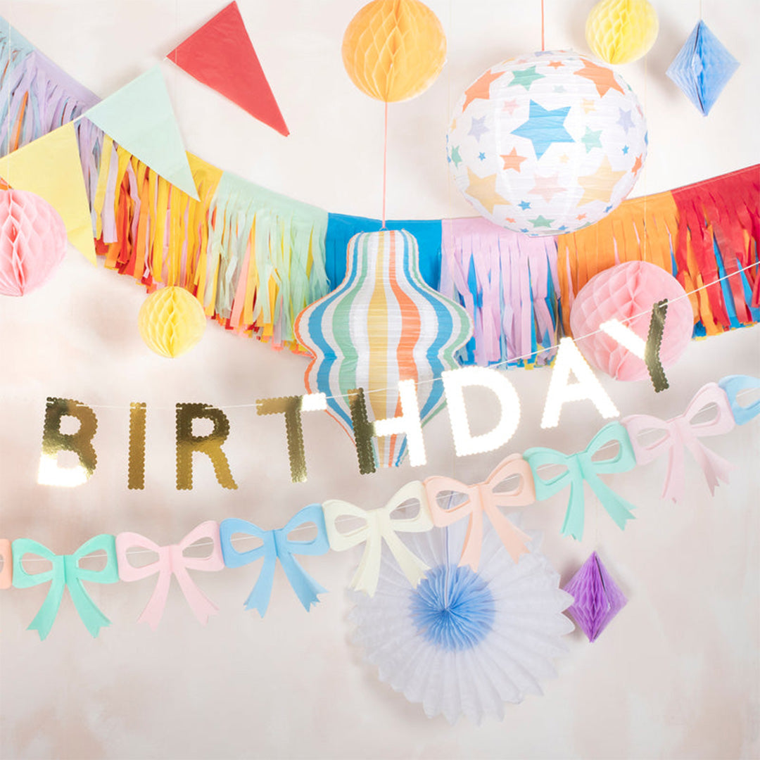 Feestelijke Meri Meri decoratie met diverse slingers, waaronder vlaggetjes en een 'BIRTHDAY' banner, en honingraatdecoraties.