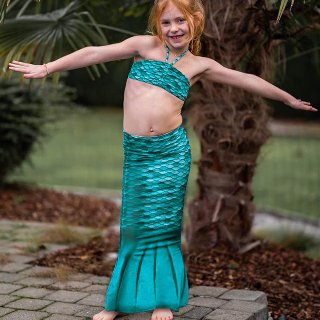 Een meisje draagt de turquoise zeemeerminstaart en bikinitop in een tuin.