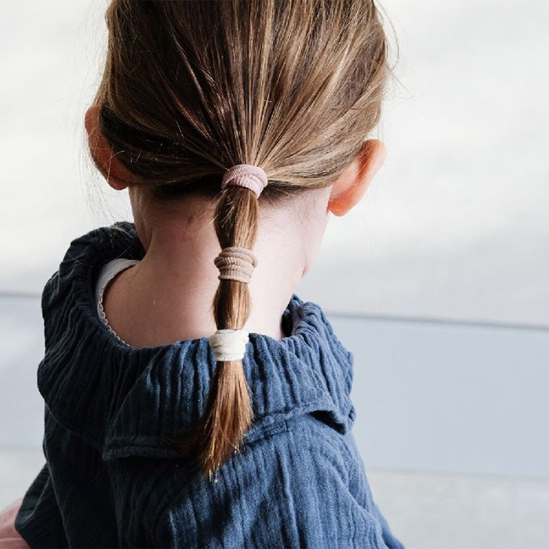 Een kind met bruin haar, vastgebonden in een staart met drie mimi & lula badstof haarelastiekjes.