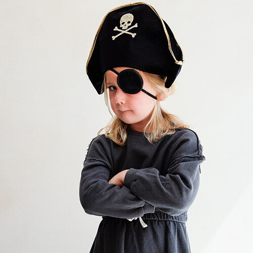 Een kind met de mimi & lula piratenhoed en ooglapje kijkt serieus met gekruiste armen.