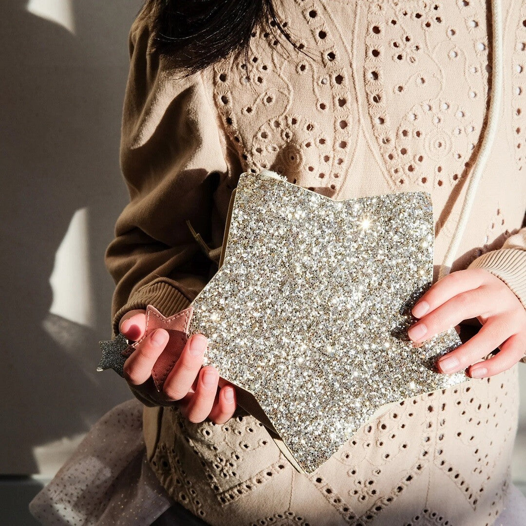 Detailfoto van kinderhanden die een zilveren glitter schoudertasje in de vorm van een ster vasthouden.