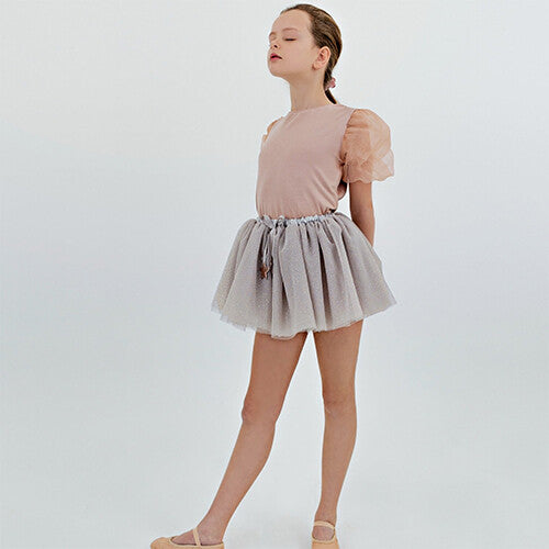 Meisje staat in de mimi & lula grijze tule kinderrok met een roze top en balletschoenen.