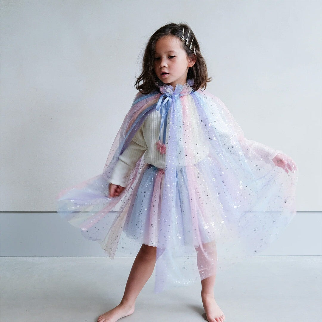 Een kind draagt de mimi & lula tule regenboogrok en een bijpassende cape met sterren.