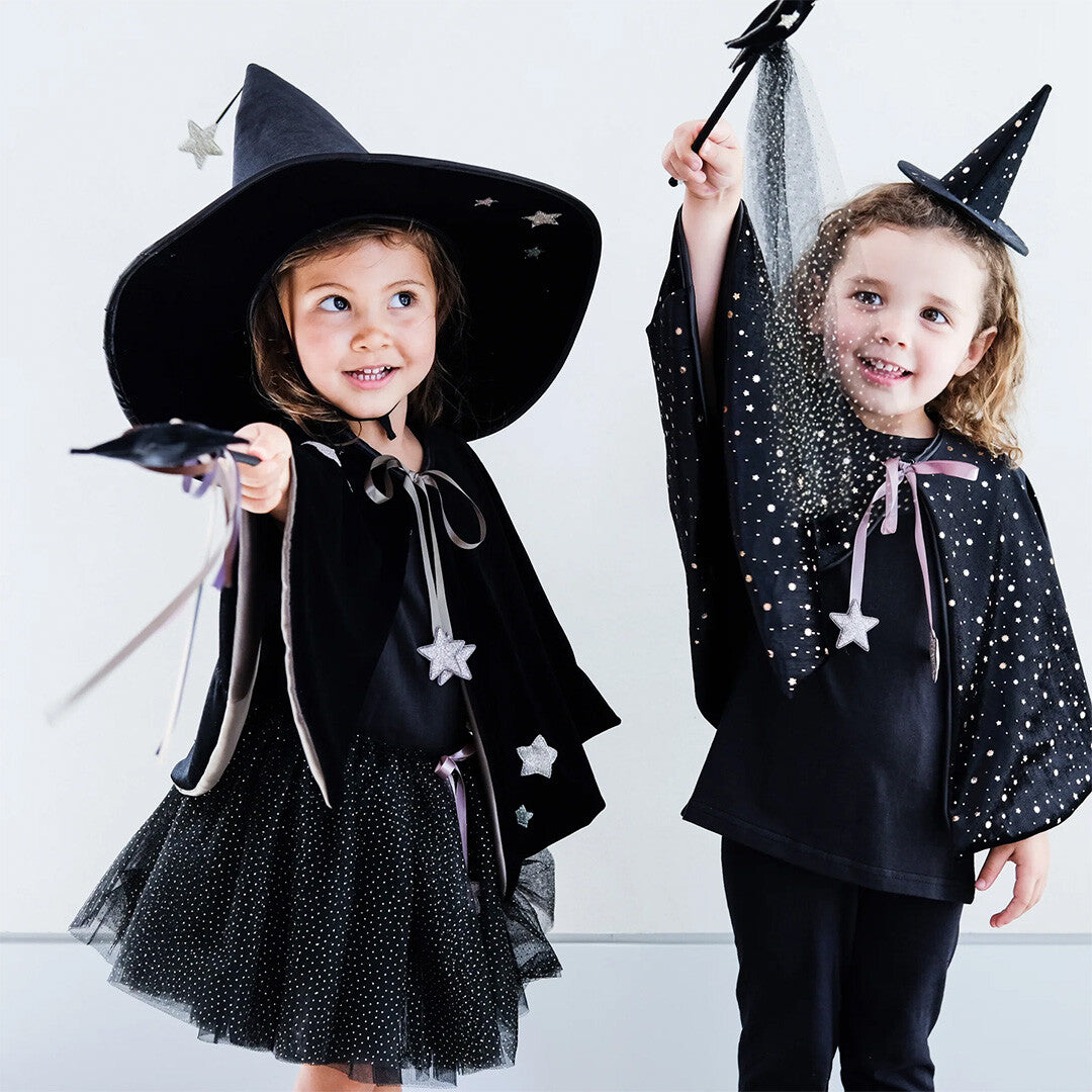 Twee meisjes verkleed als heksen met zwarte capes en sterren, waarvan één glitter strooit.