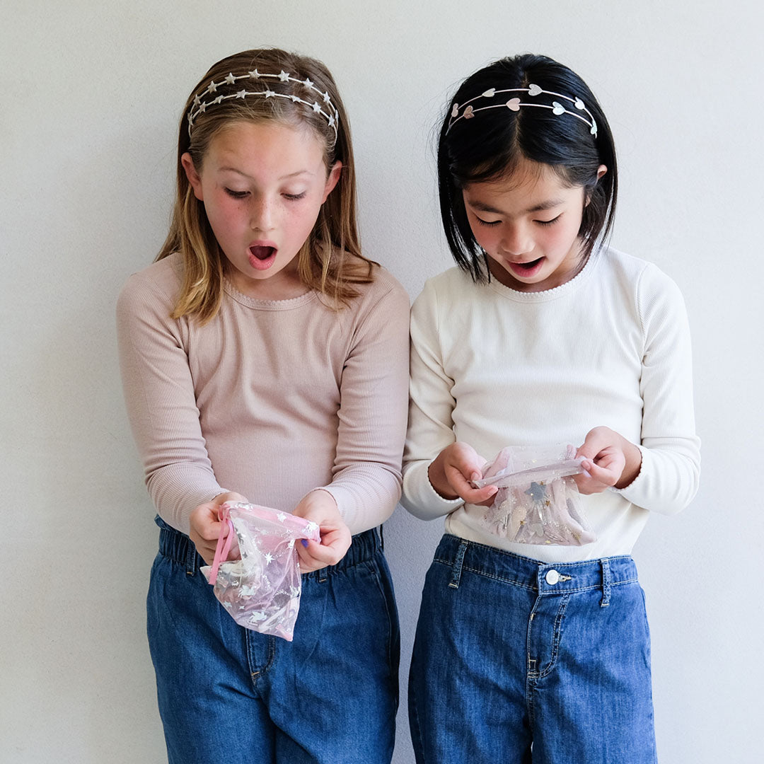 Twee meisjes kijken verrast naar de mimi & lula haaraccessoires in hun transparante zakjes.