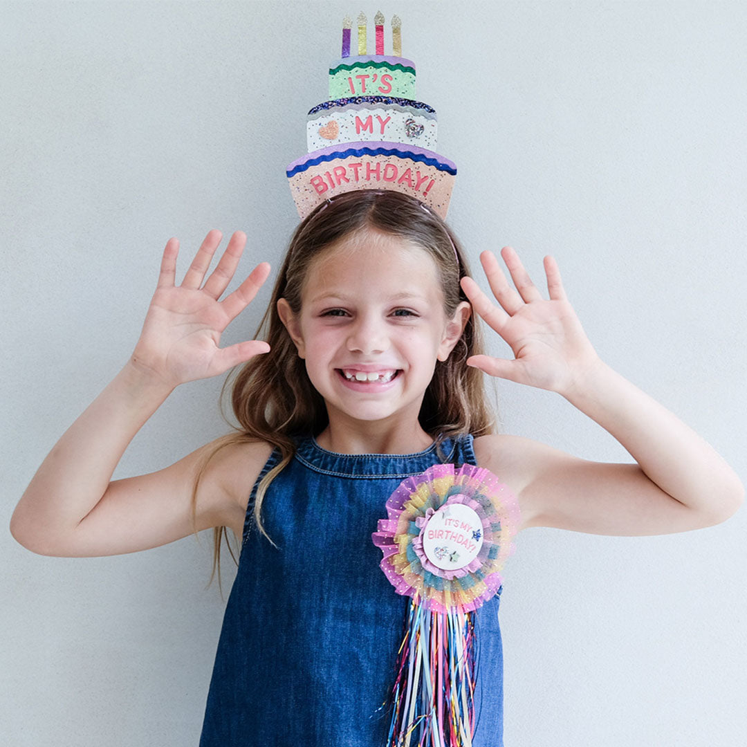 Een lachend kind draagt de Mimi & Lula verjaardagstaart hoofdband en een bijpassende "It's My Birthday!" badge.