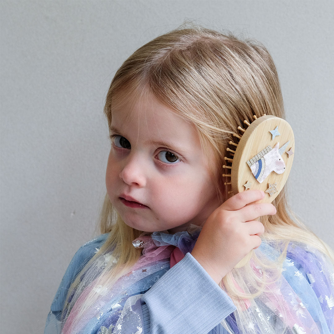 Een jong meisje borstelt haar blonde haar met de mimi & lula houten kinderhaarborstel met eenhoorn.