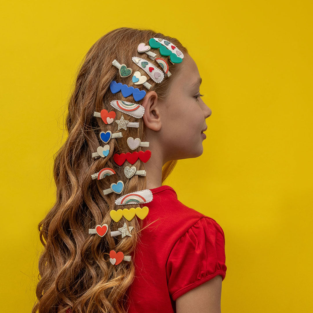 Zijzicht van een kind met lang haar, versierd met mimi & lula haarclipjes met regenboog-, hart- en stervormen.