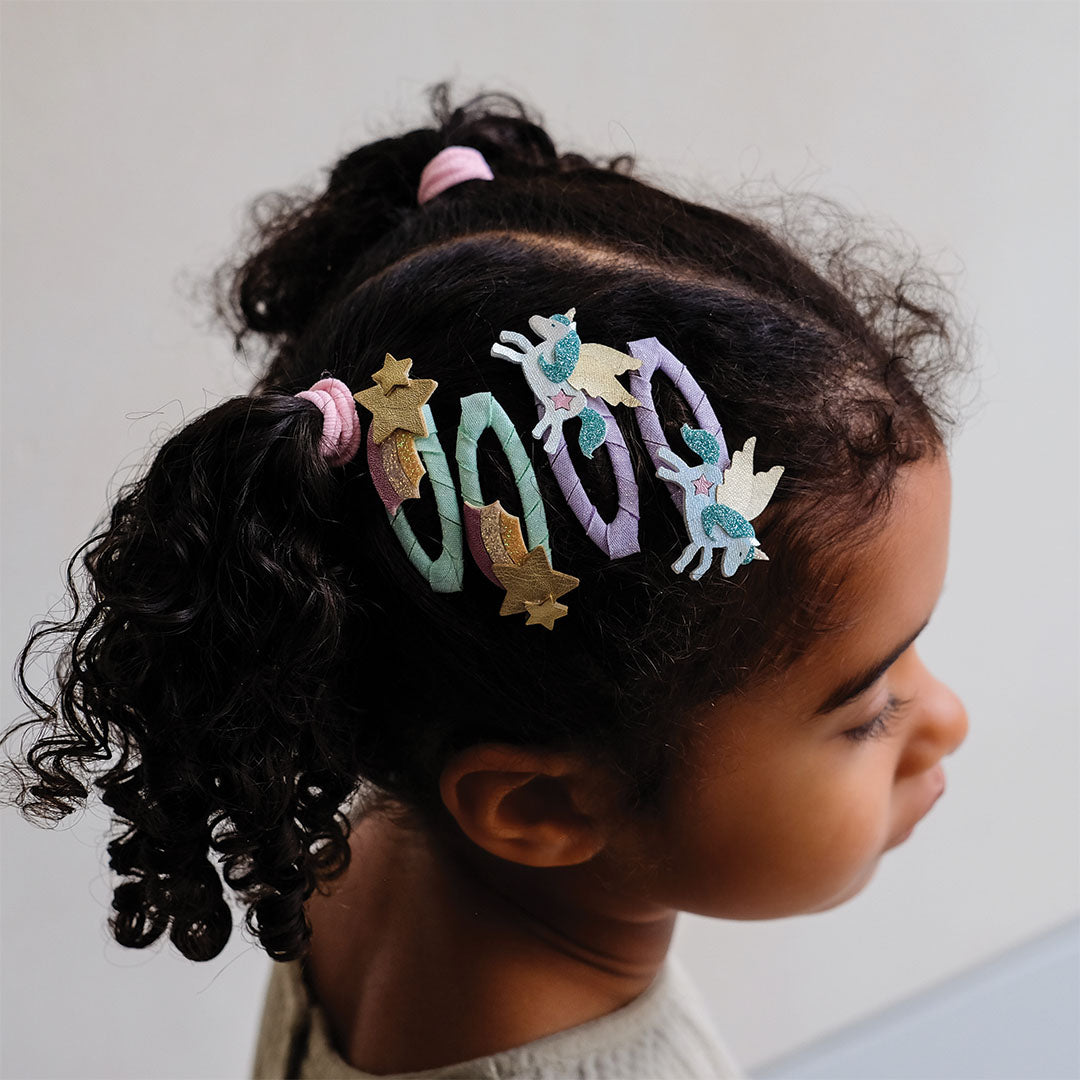 Een kind draagt de mimi & lula haarspeldjes met eenhoorns, sterren en regenbogen in haar haar.