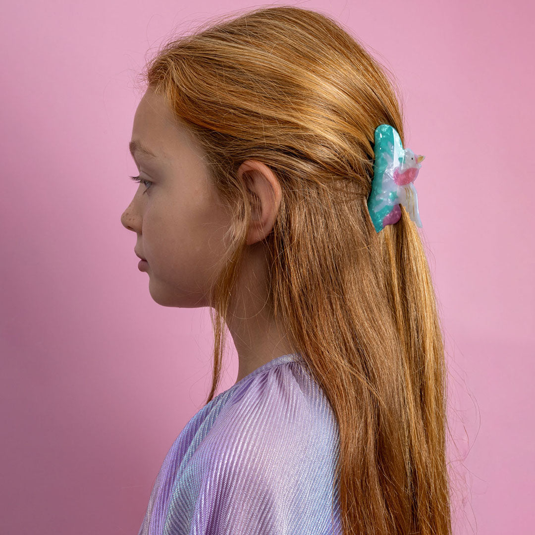 Een meisje met lang roodbruin haar draagt de mimi & lula eenhoorn haarclip aan de zijkant van haar hoofd.