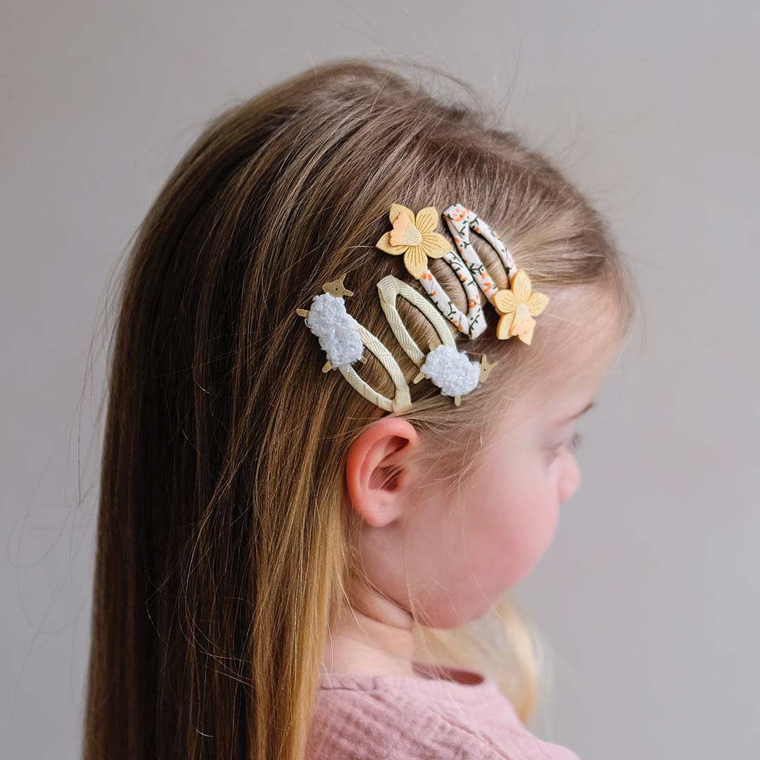 Een kind met lang haar draagt de Mimi & Lula haarspeldjes met lammetjes en bloemen.